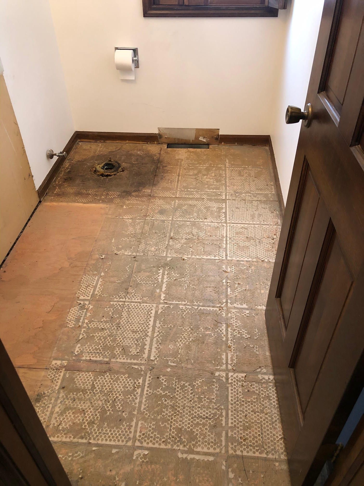Bathroom floor with a large section of missing tile and exposed subfloor near the toilet area