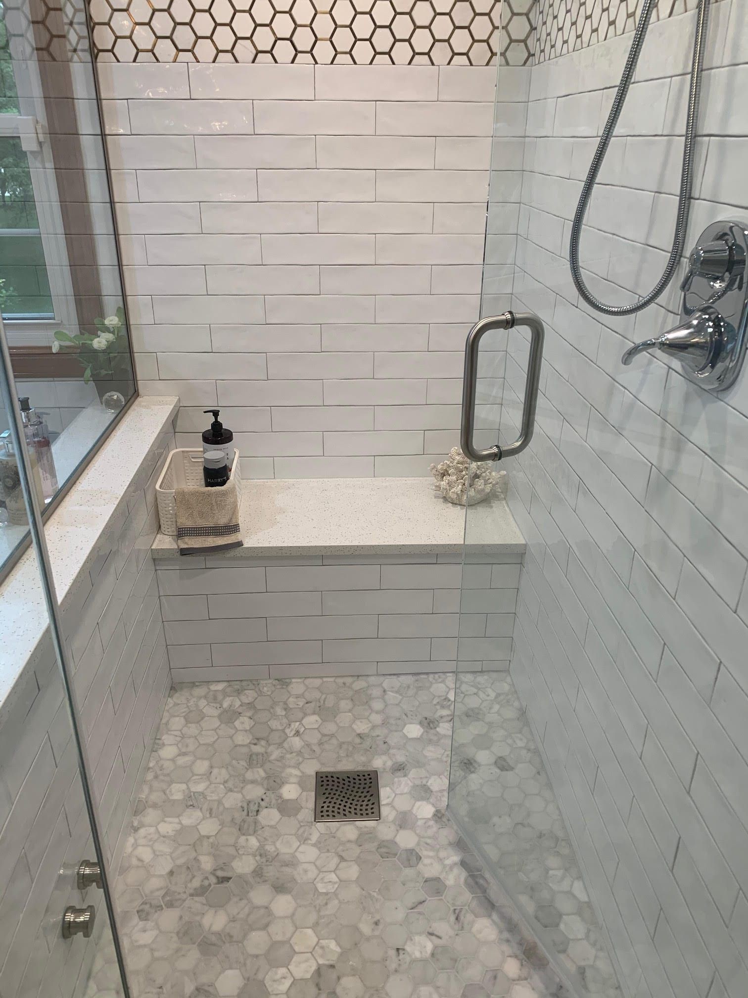 Glass shower with hex tile floor, white subway-tile wall, bench, grab bar, and shower controls