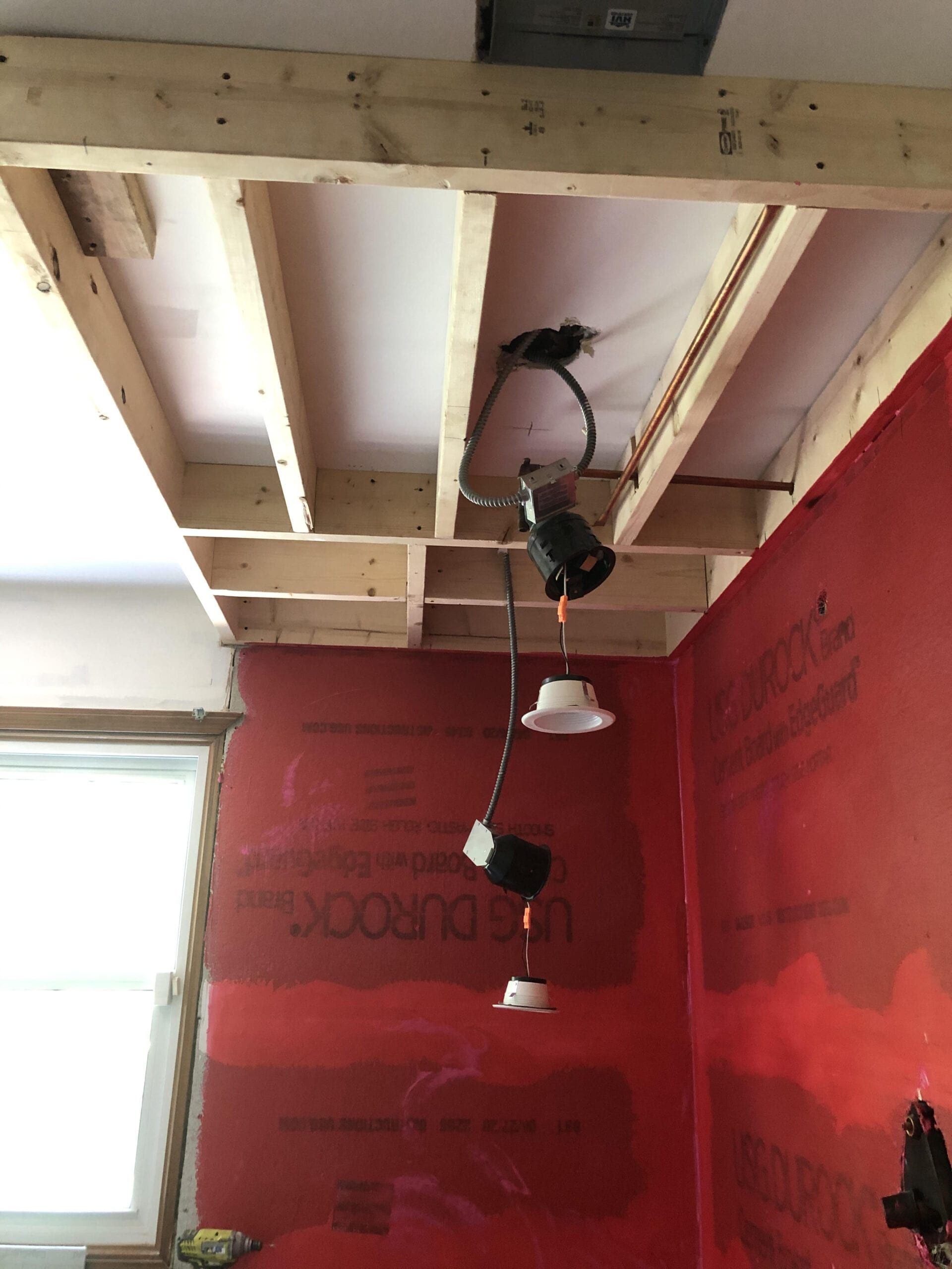 Unfinished room with red walls, exposed ceiling beams, hanging track lights, and a bright window.