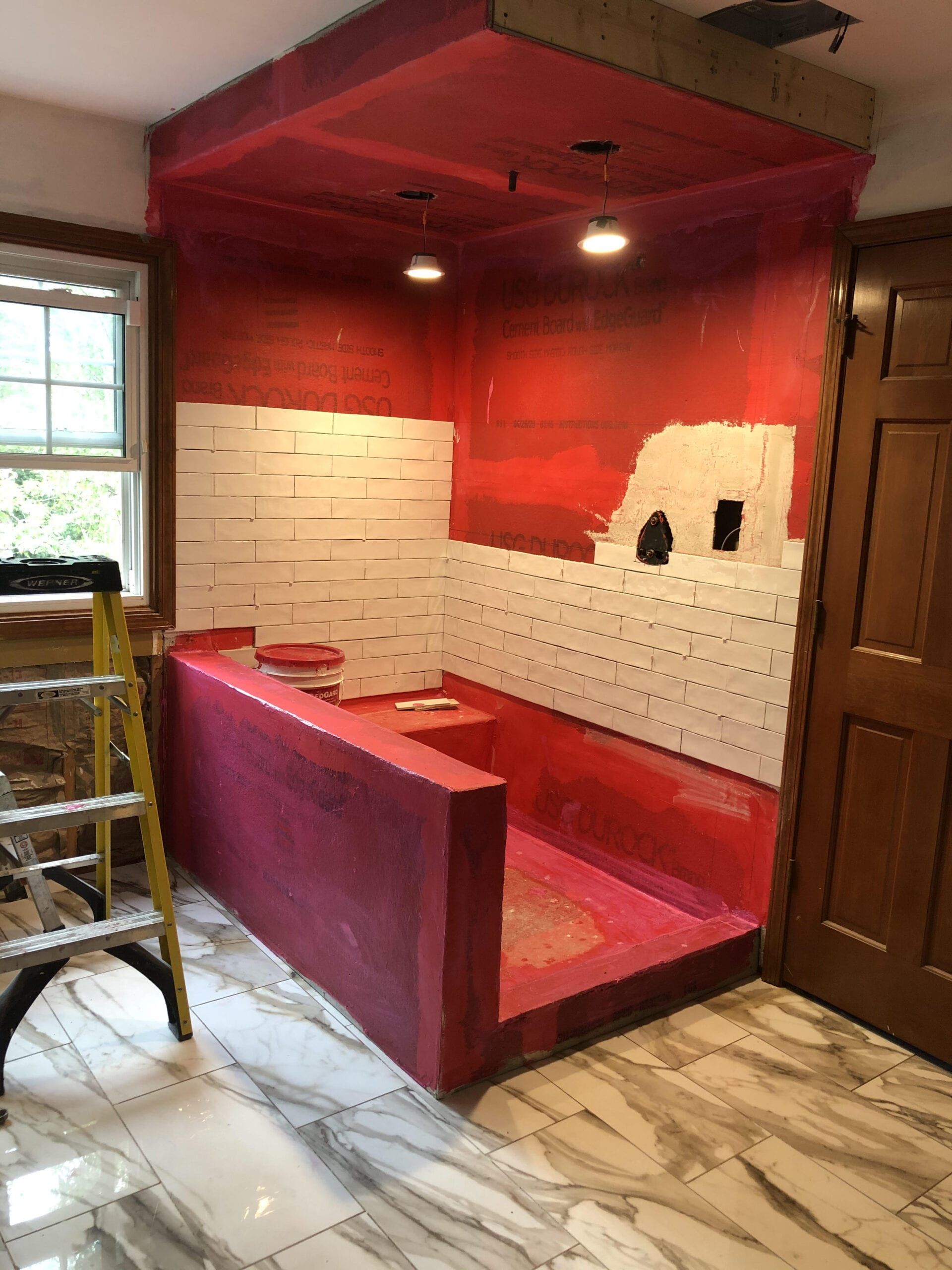 Red kitchen nook with unfinished white tile backsplash, pink bench seating, and a ladder on the left