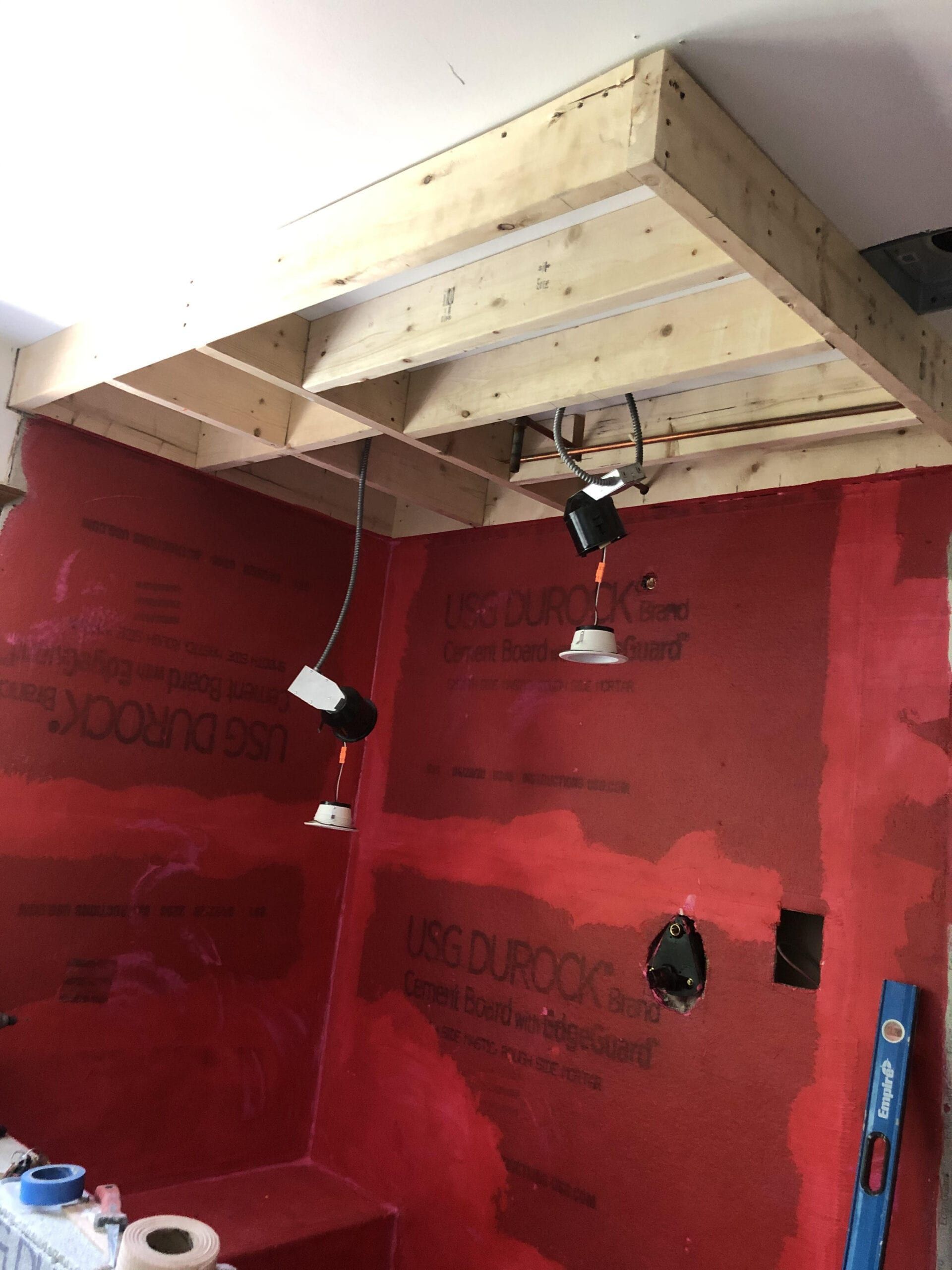 Bathroom shower under renovation with red waterproof wall panels and exposed wooden ceiling framing.