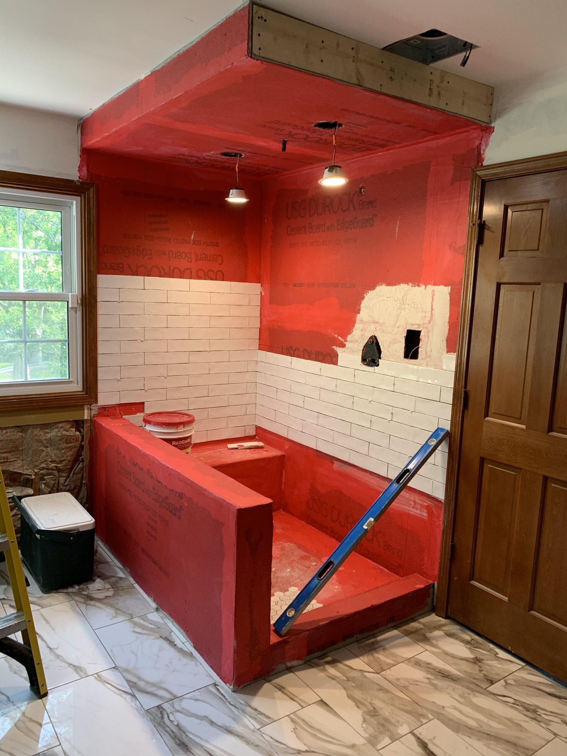 Red-tiled shower under renovation with white walls, red bench, and blue support pole in a bathroom.