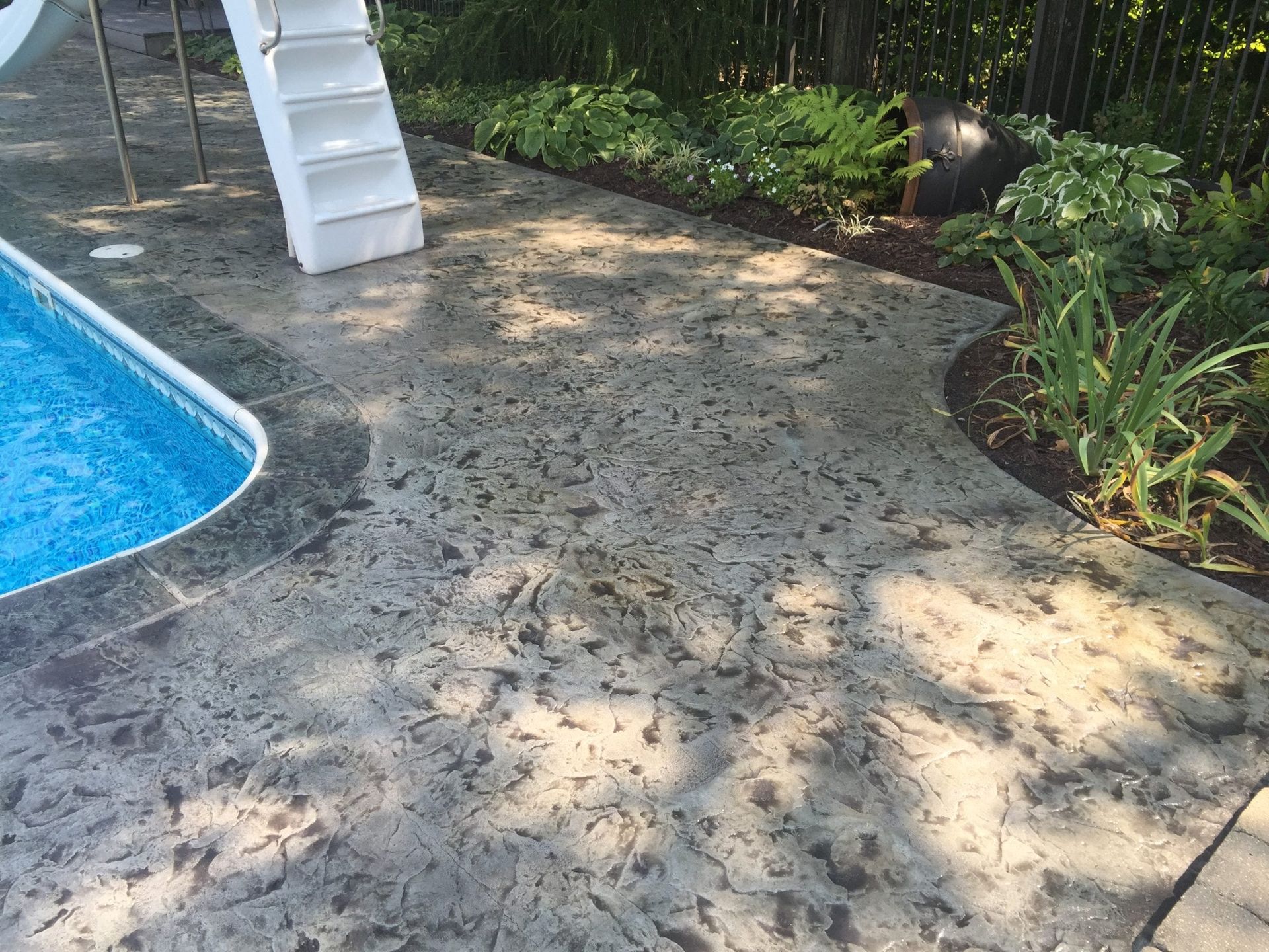 Poolside patio with white chair, blue pool edge, and sunlit plants along a paved walkway