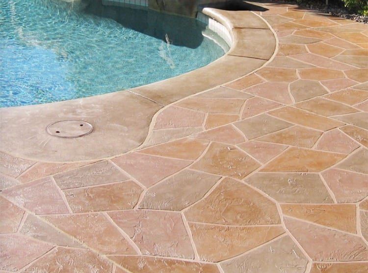 Curved pool edge with blue water beside tan stone patio paving