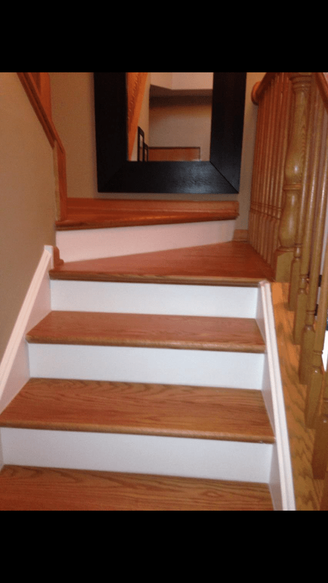 Indoor staircase with white risers, wooden steps, and a wooden railing leading to a hallway mirror
