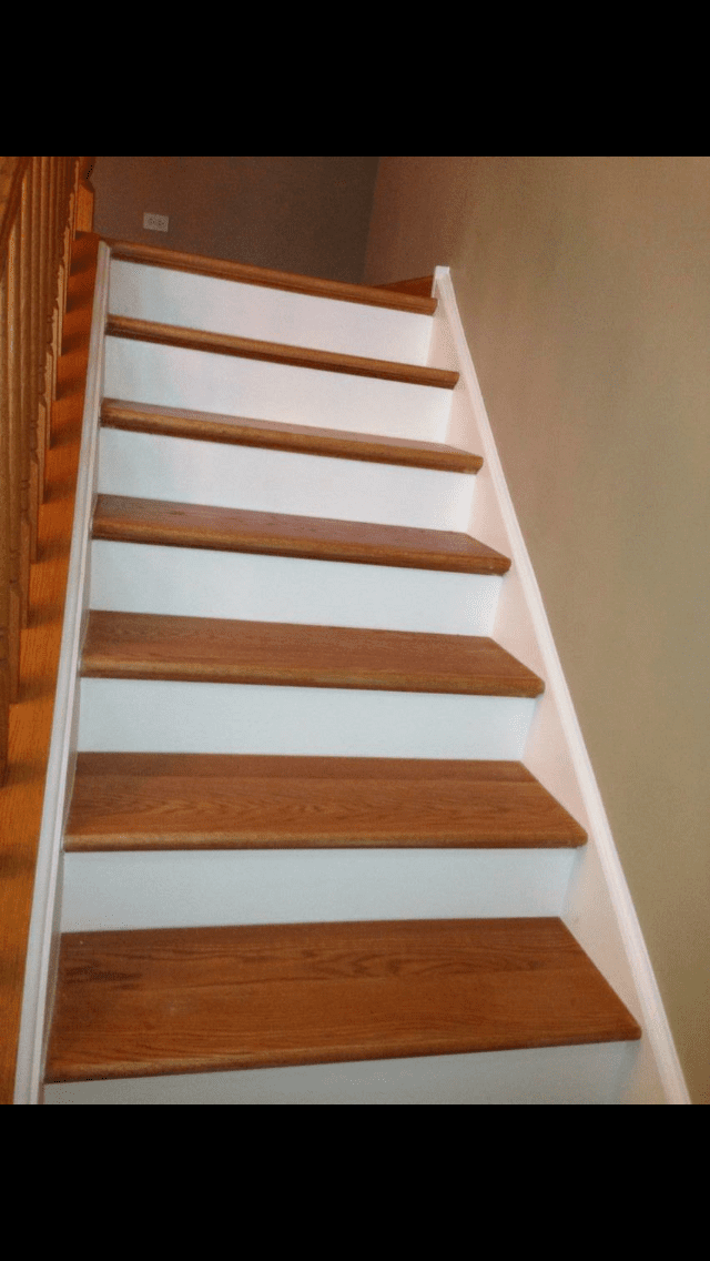 Wooden staircase with white railings and brown steps against beige walls.