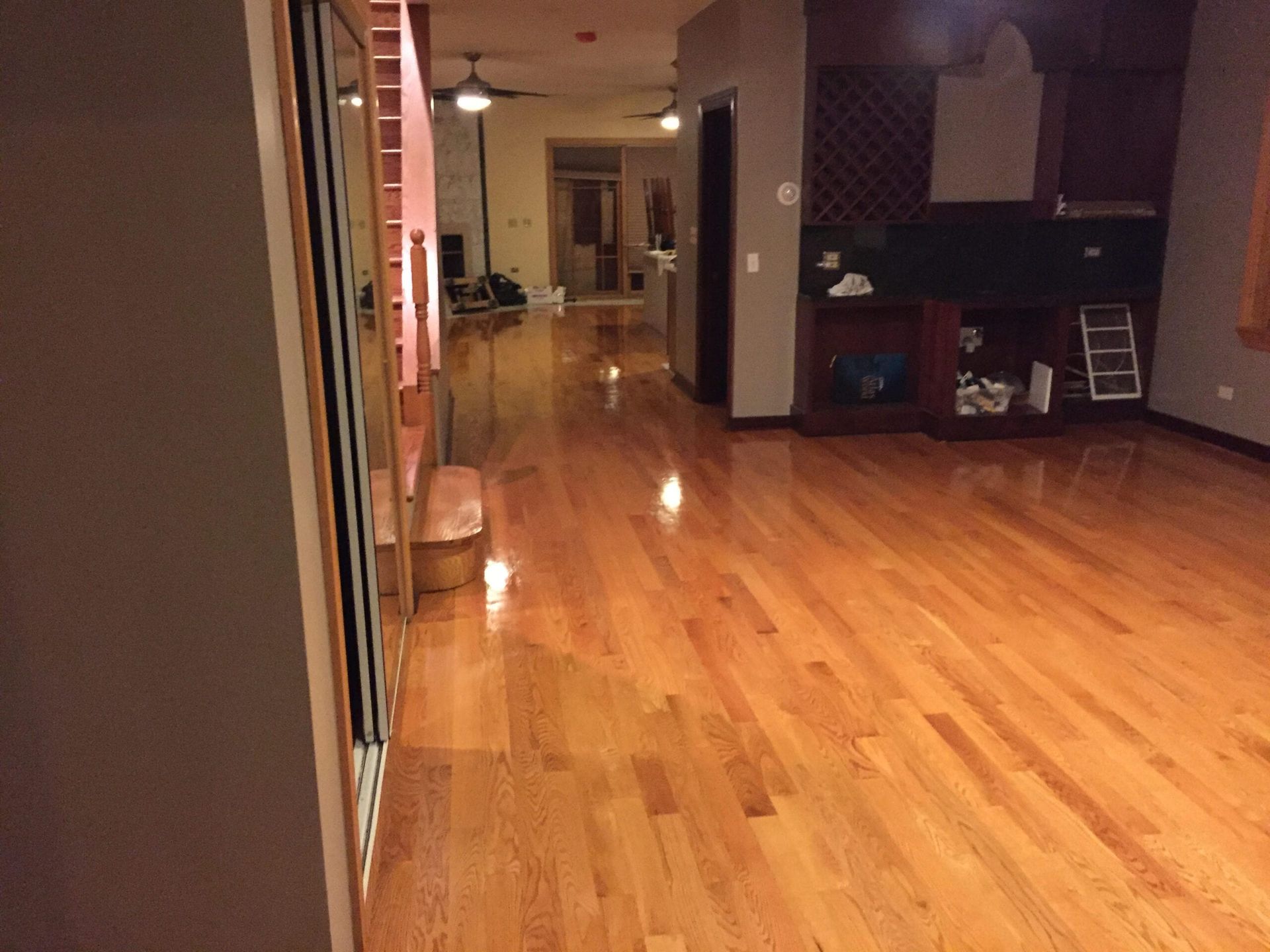 Empty indoor hallway with polished wood floors and warm lighting leading to a kitchen and living area