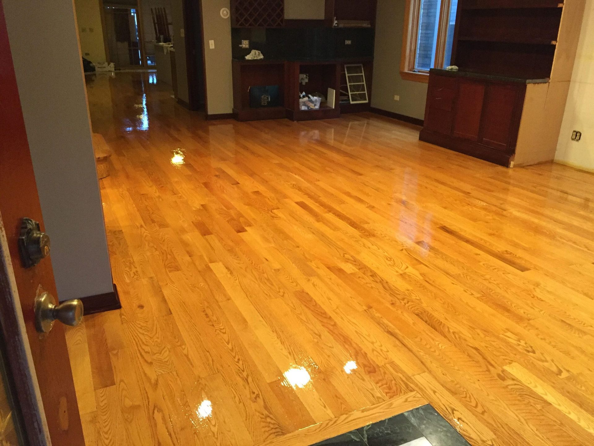 Empty room with shiny hardwood floors, built-in shelves, and a window with blinds.