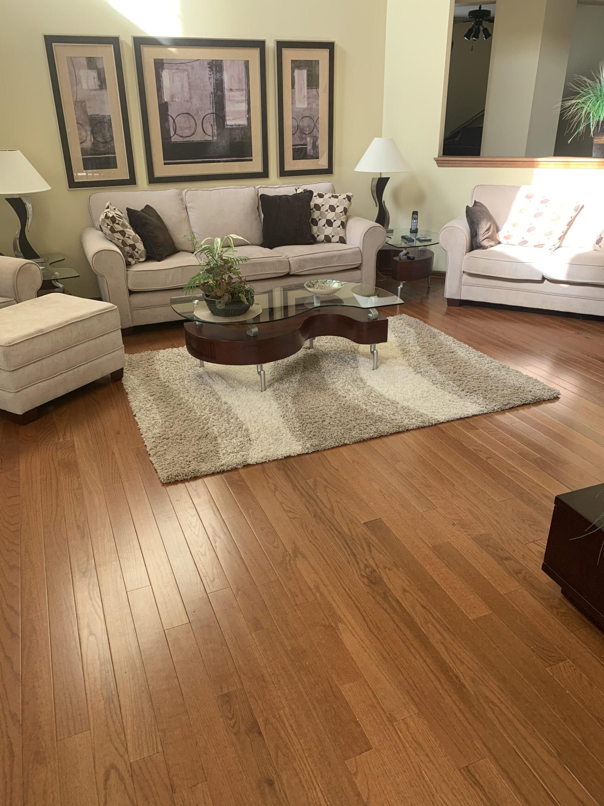 Cozy living room with beige sofas, patterned chairs, coffee table, lamp, framed art, and hardwood floor