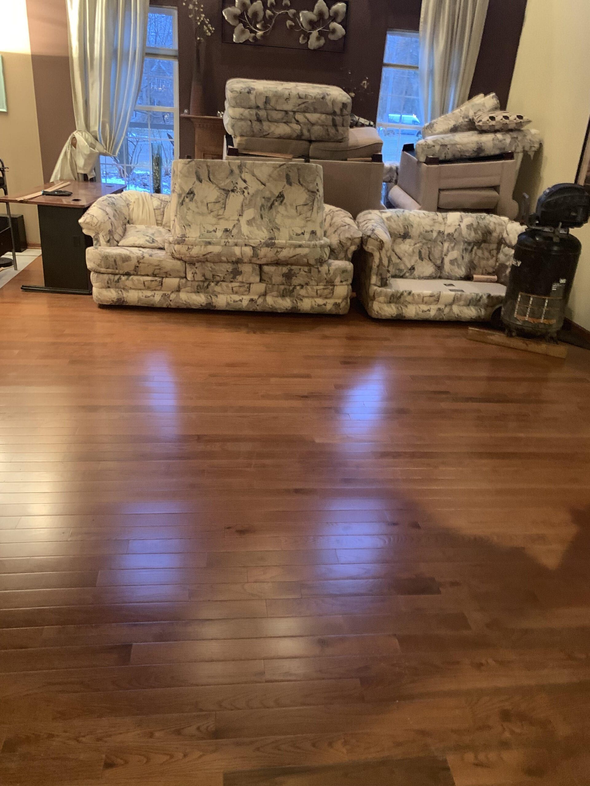 Living room with patterned sofas, a window, and polished hardwood floor