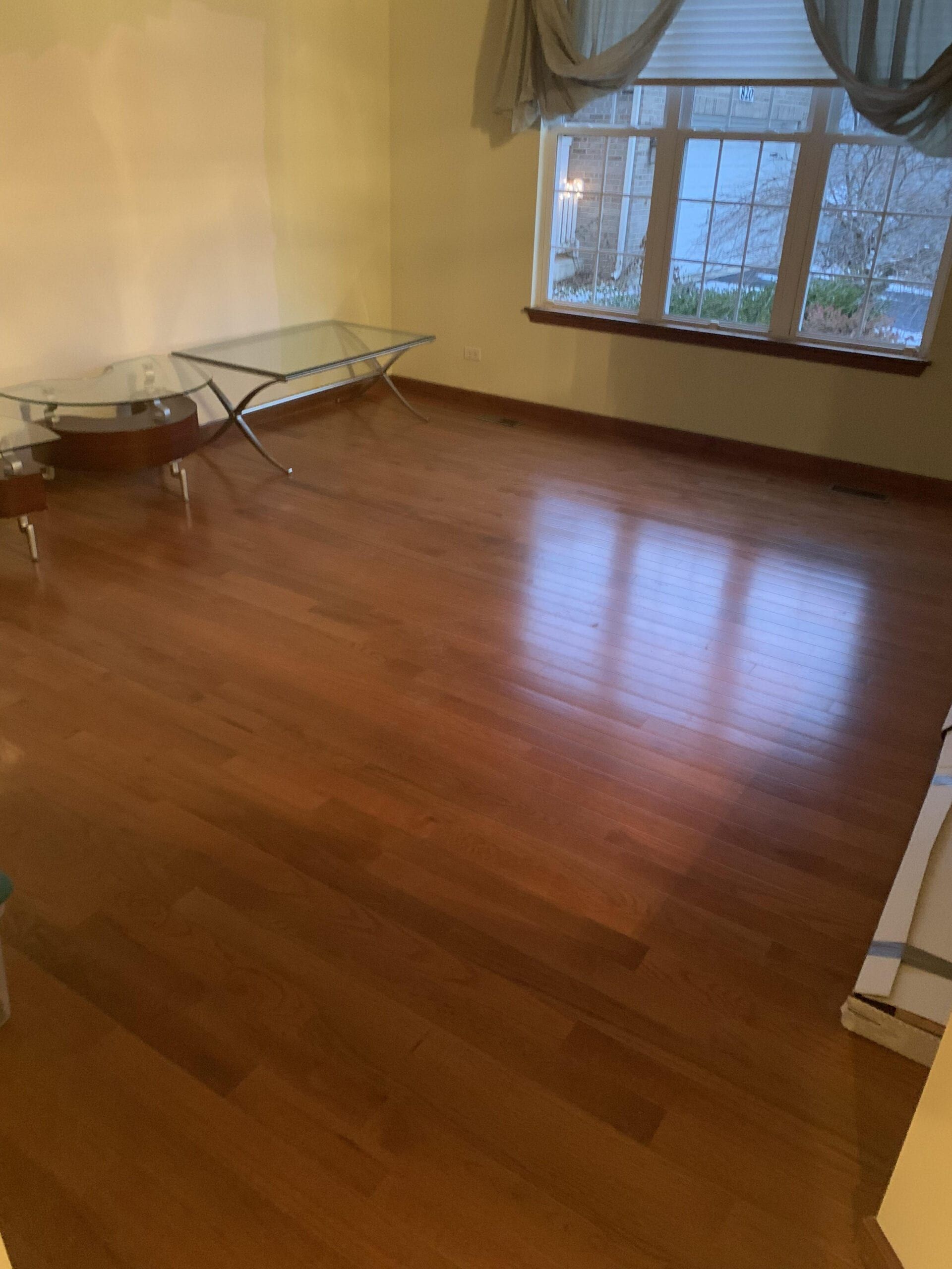 Empty room with polished wooden floor, window, and folding table against the wall