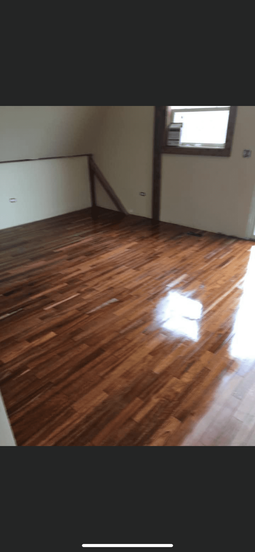 Empty room with glossy wood floors, white walls, and a small window letting in light.