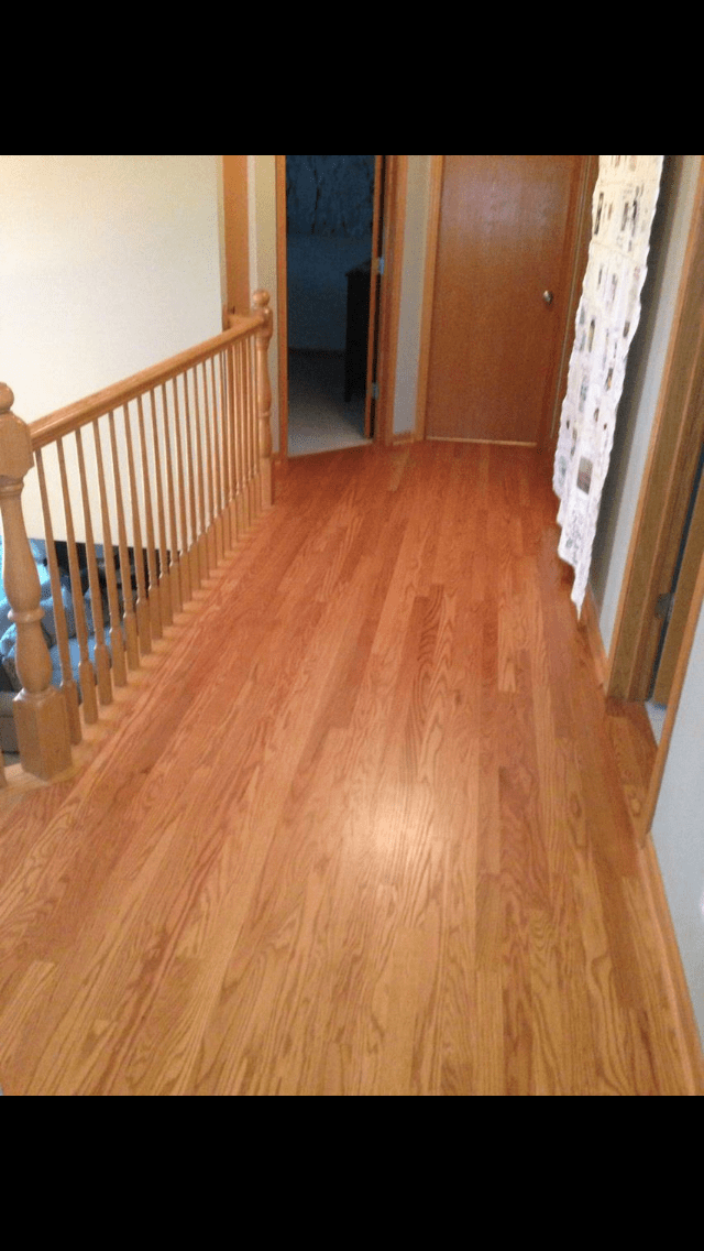 Hallway with hardwood floor, wooden railing, and open doors leading to a darker room