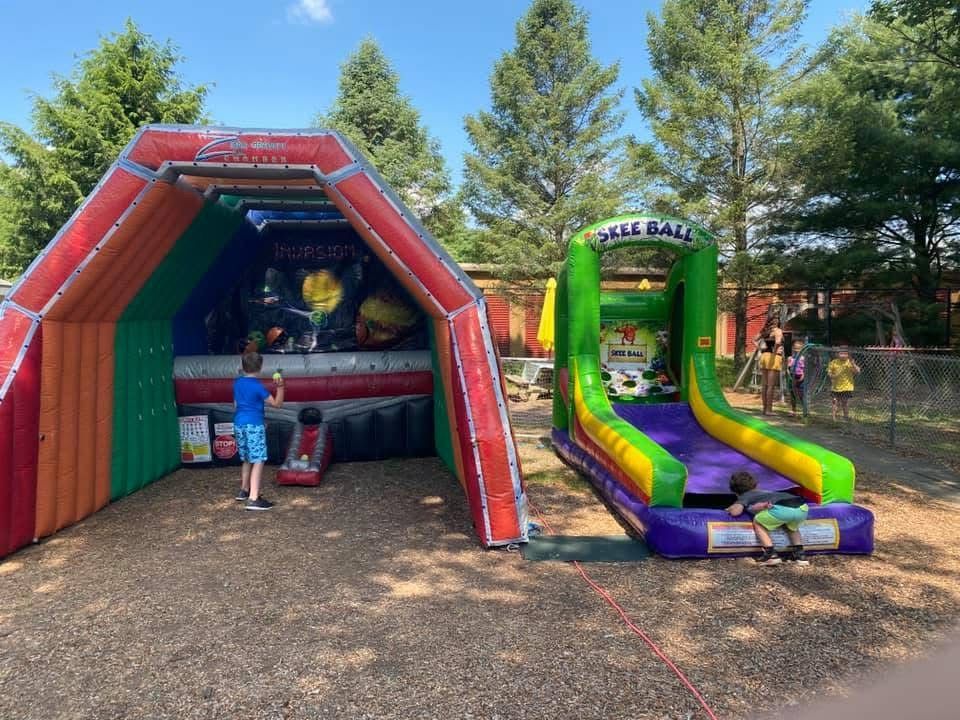 Colorful inflatable arcade and slide booths in a park, with a child playing under sunny trees.