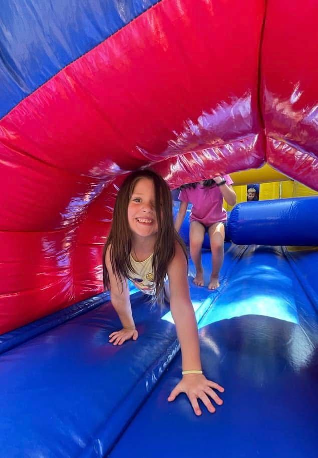Child crawling through a colorful inflatable tunnel with another child behind her