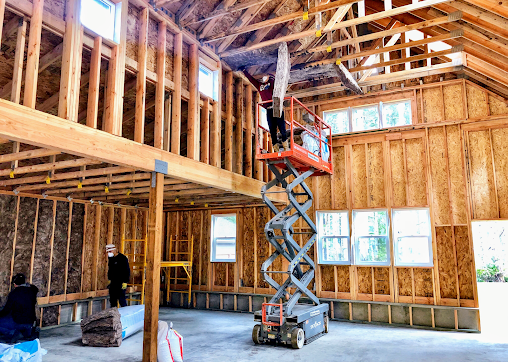 A man is standing on a scissor lift in a building under construction.