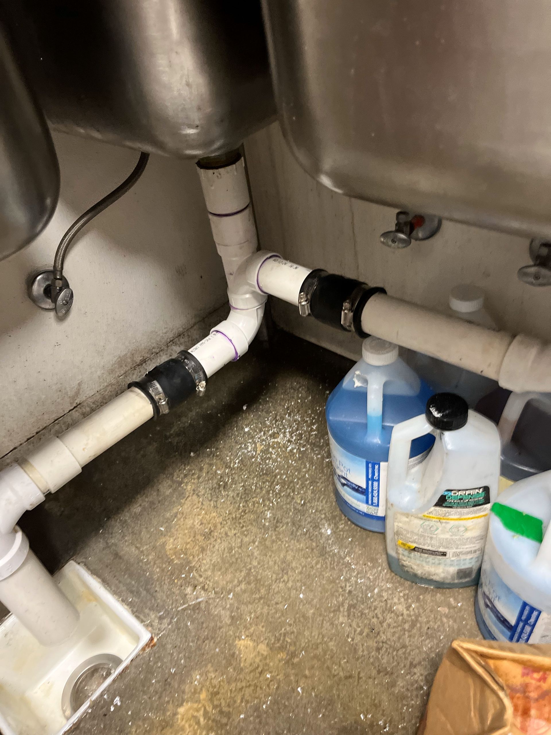 A kitchen sink with bottles of cleaning supplies underneath it.