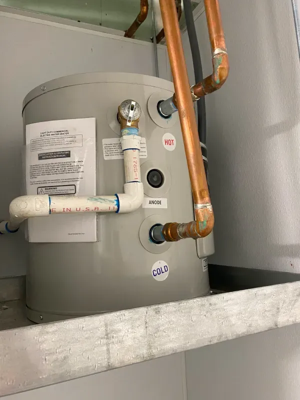 A water heater is sitting on a shelf next to copper pipes.