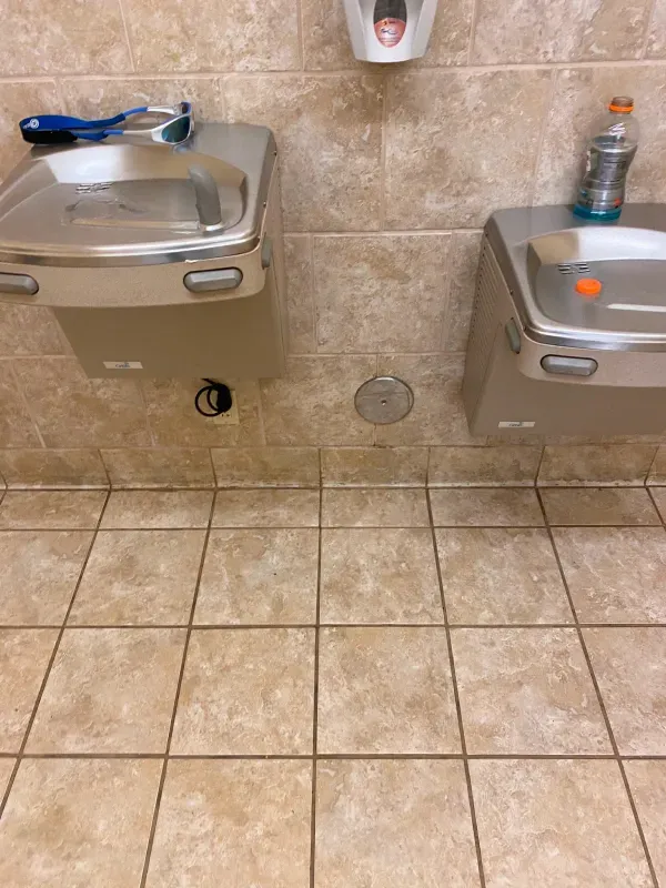 A bathroom with two sinks and a bottle of gatorade on the floor.