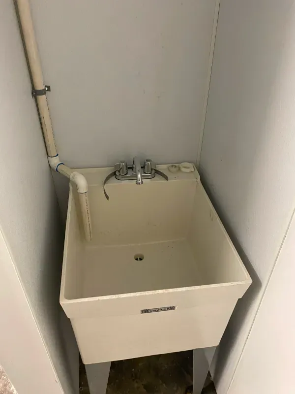 A white laundry sink is sitting in a corner of a room.