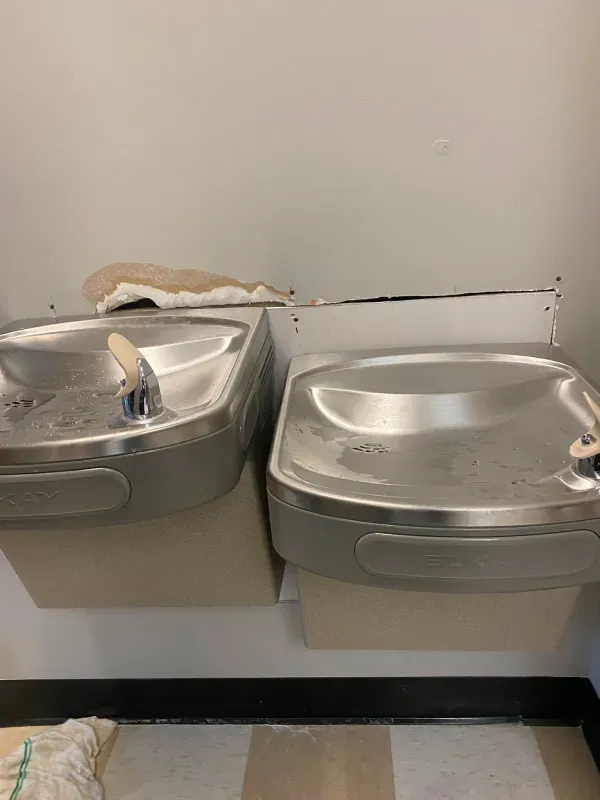 Two stainless steel water fountains are sitting next to each other in a bathroom.