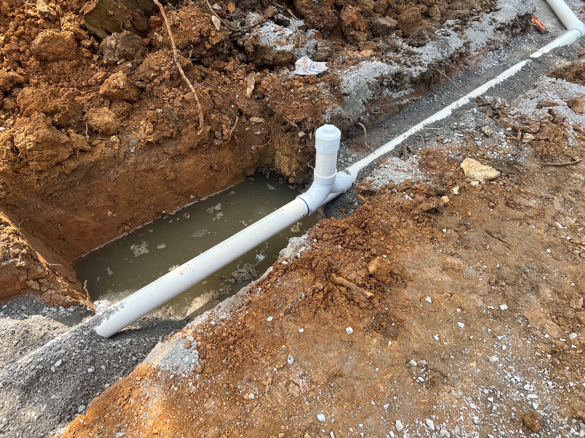 A white pipe is sitting in the dirt next to a hole in the ground.