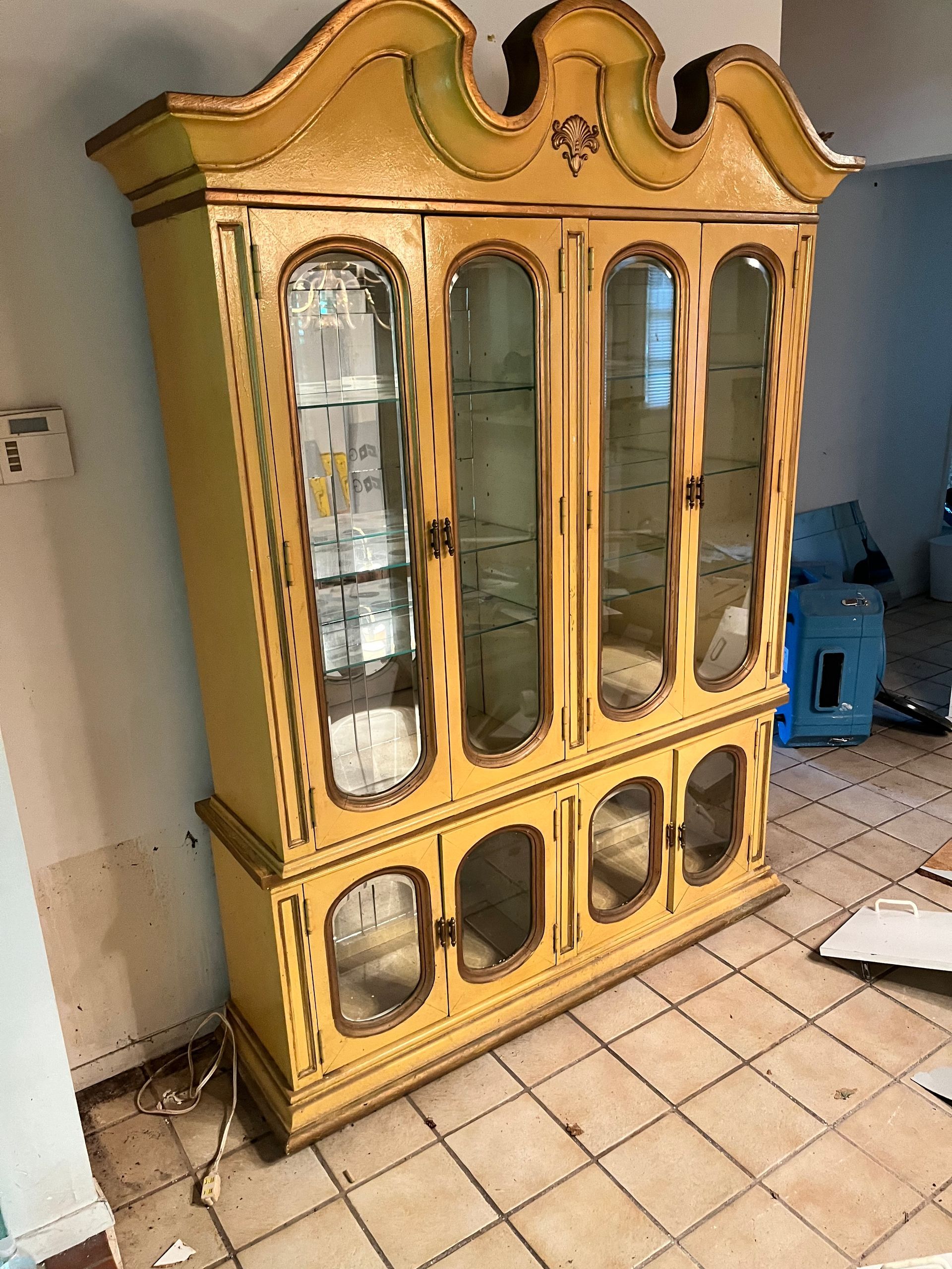 A large yellow cabinet with glass doors is sitting on a tiled floor in a room.