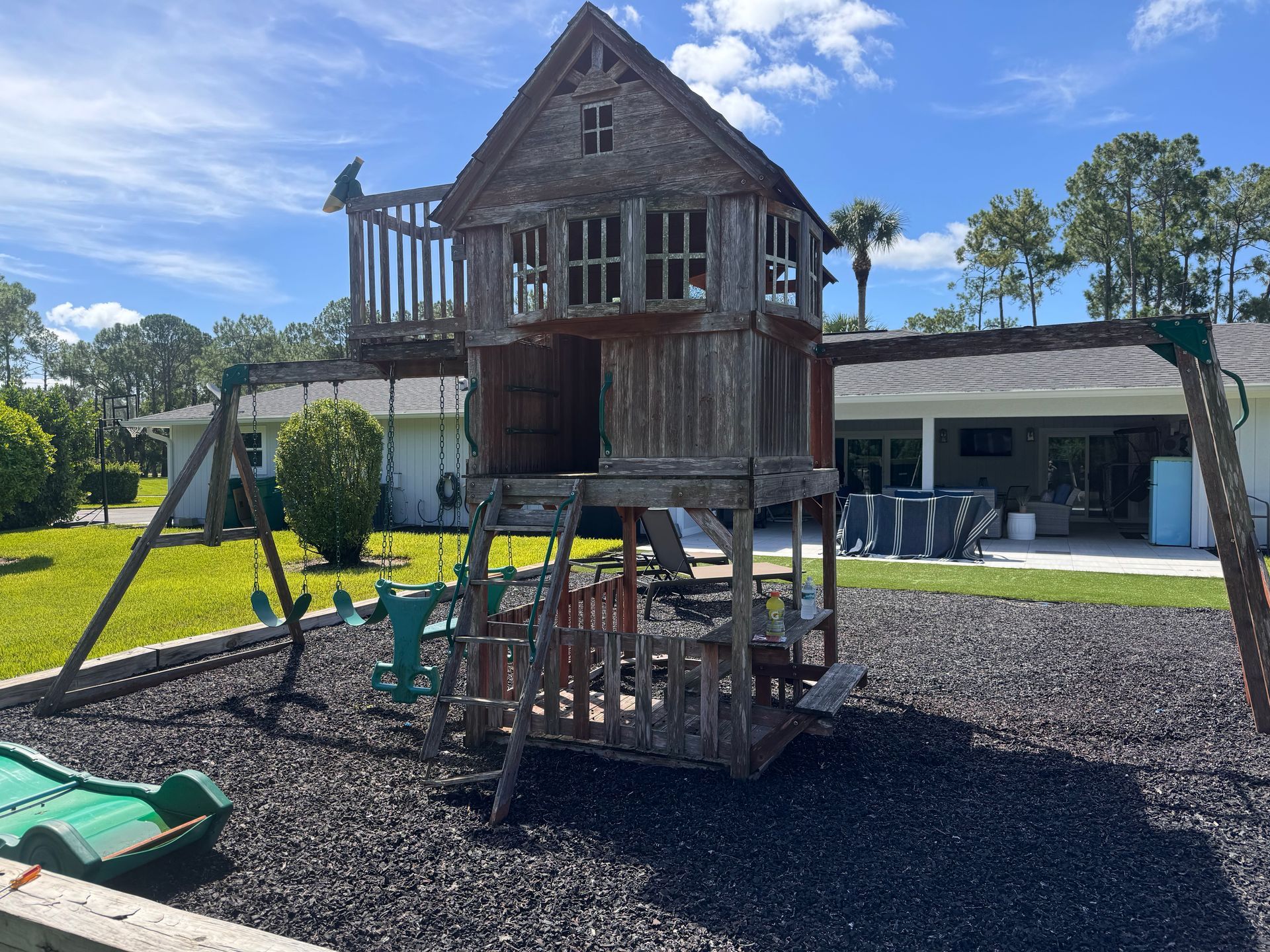 A wooden playhouse with a swing set in front of a house