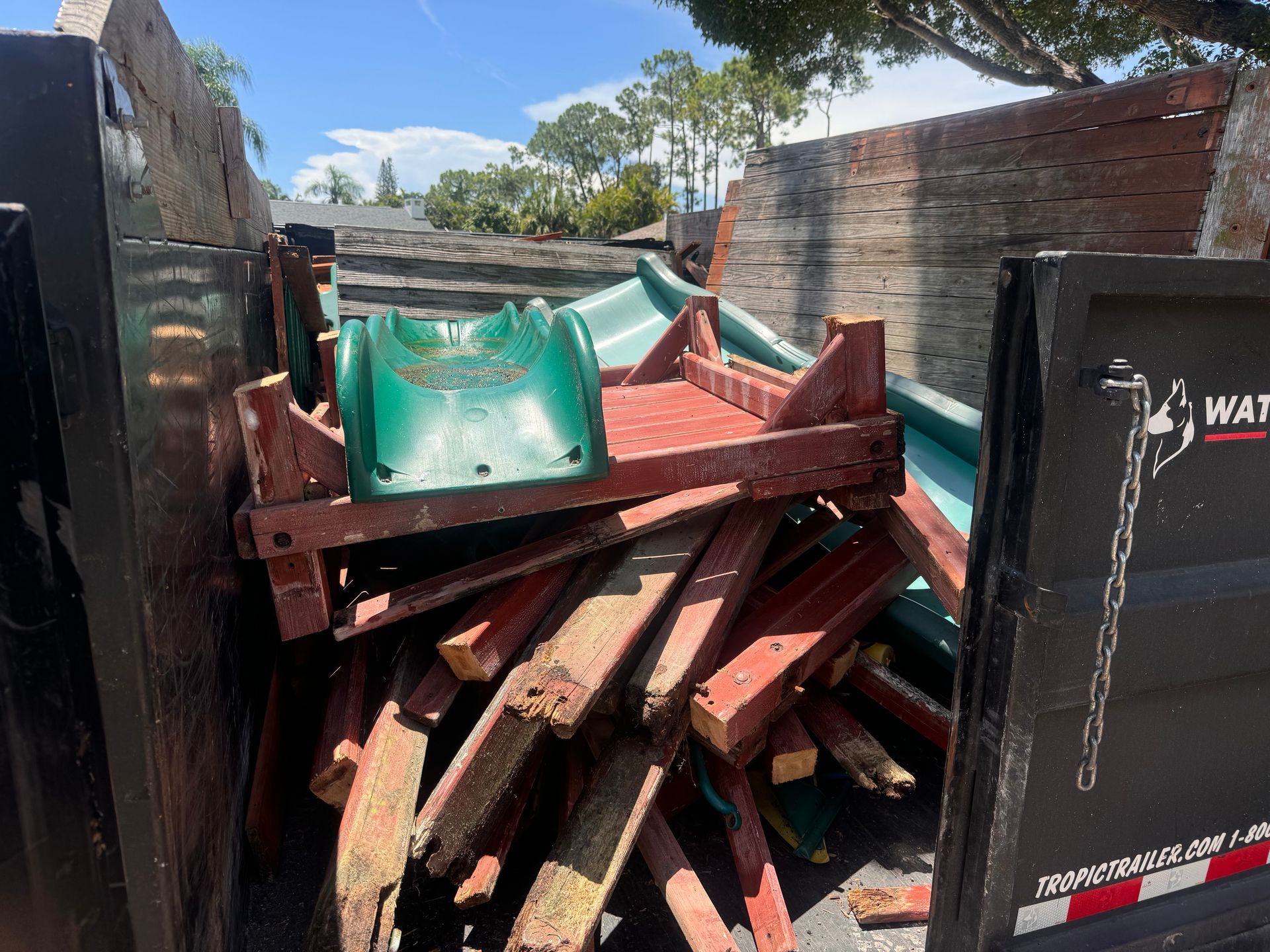 A dumpster filled with wooden pallets and a green slide.
