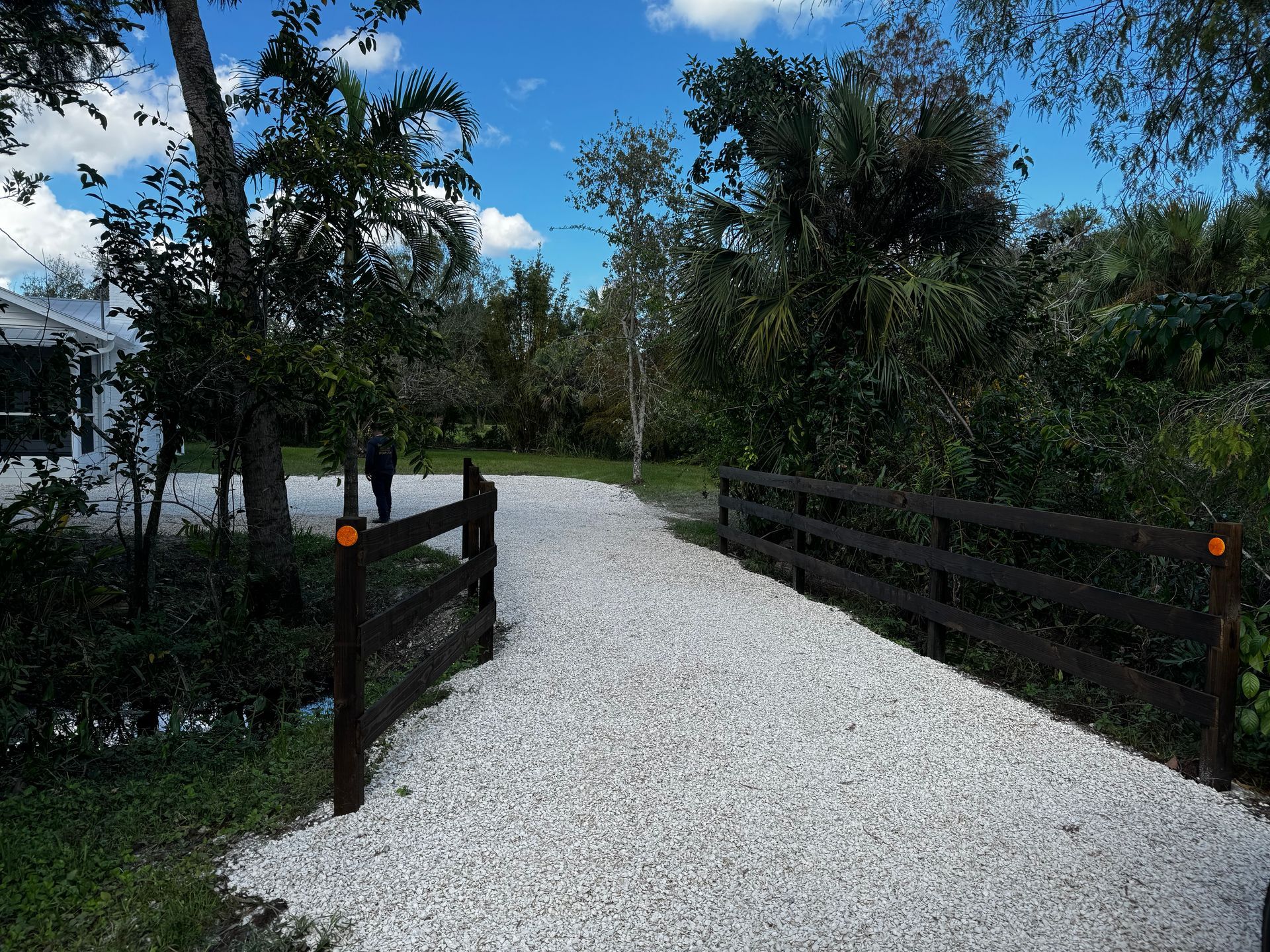 A gravel driveway leading to a house with a wooden fence