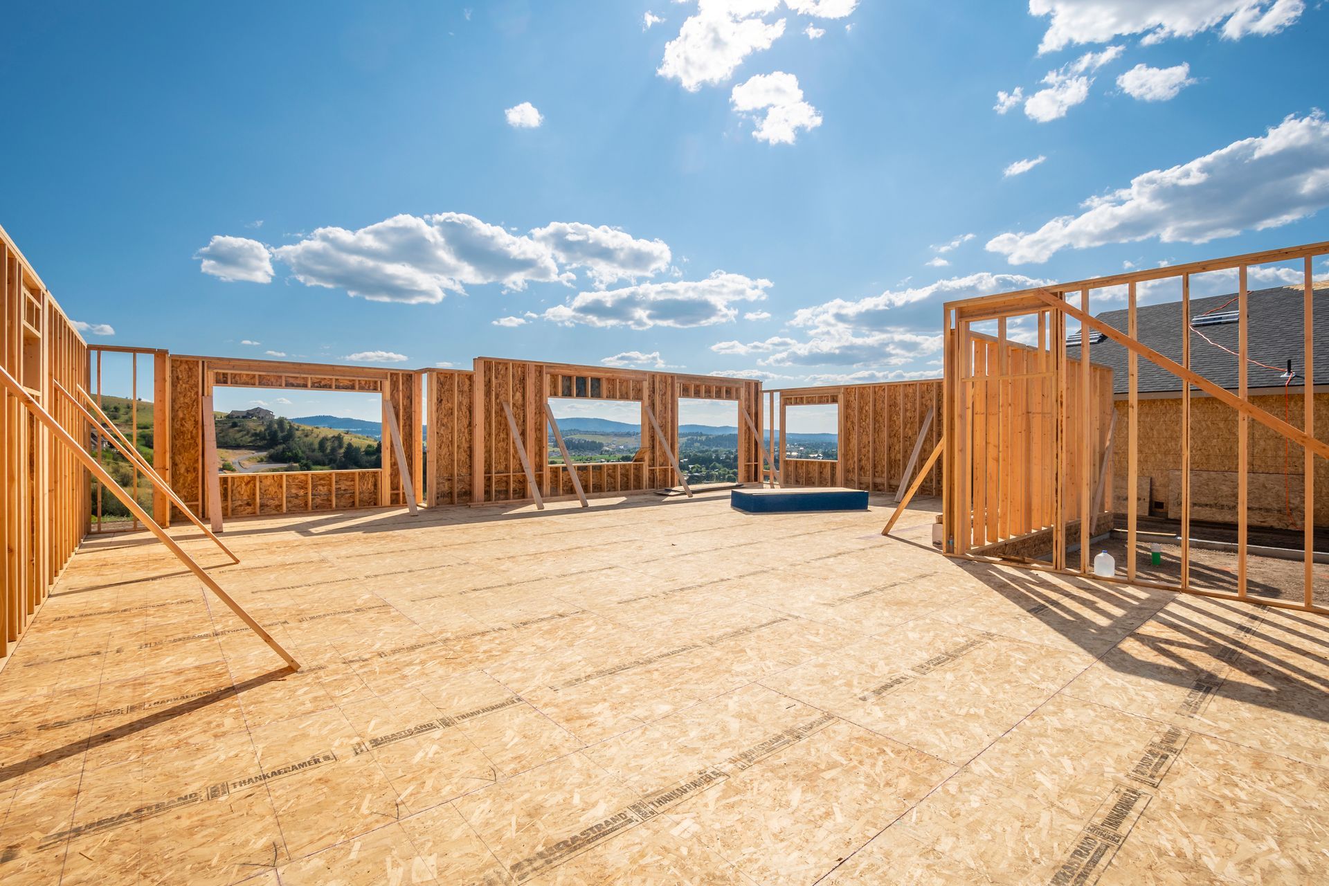 Wooden frame of a house under construction with sky and distant hills visible through window openings.