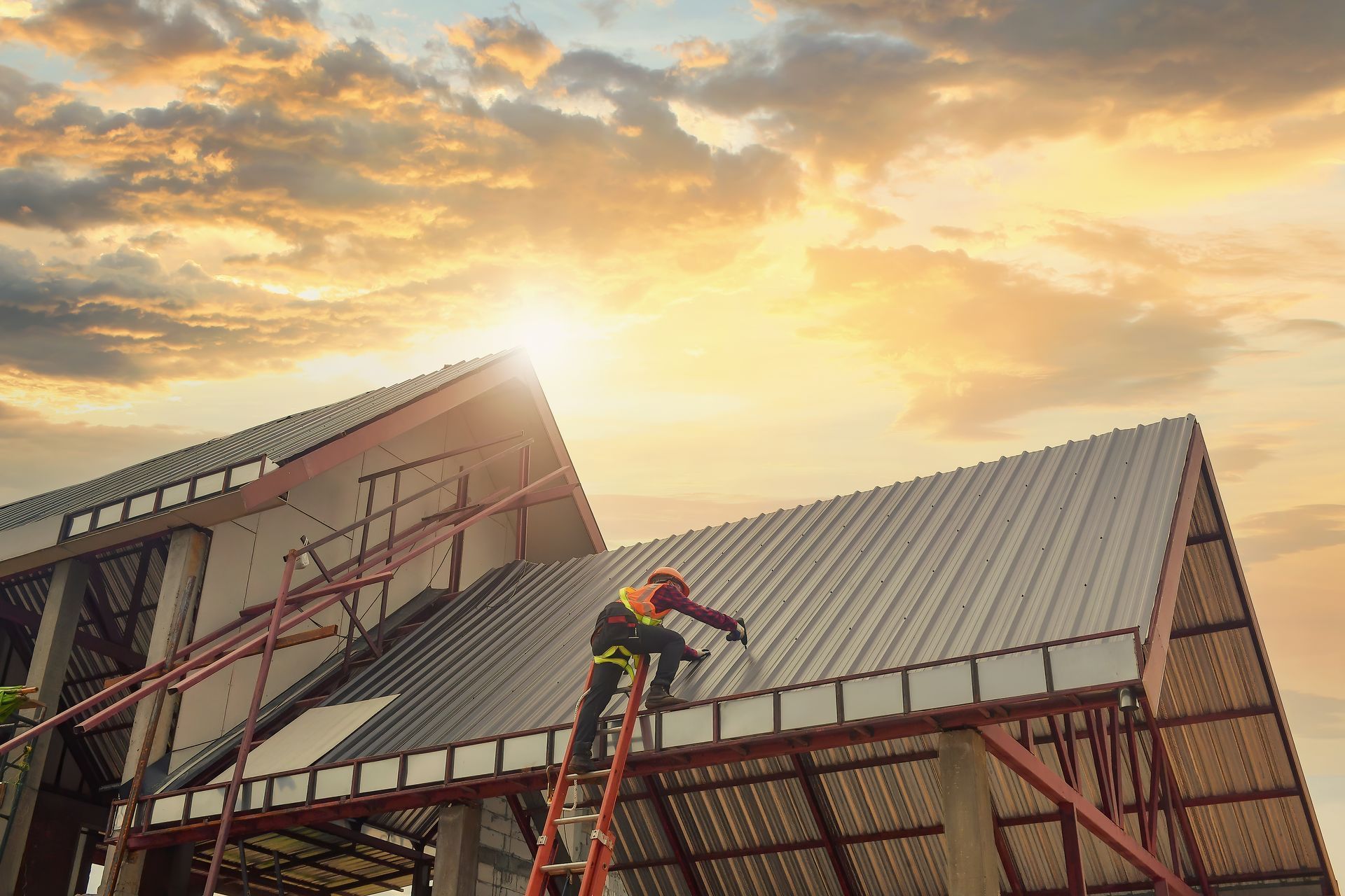 Construction workers install a metal roof on a building under a sunset.