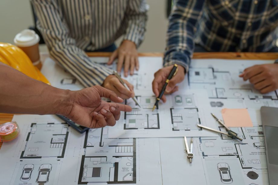 People collaborating over architectural blueprints, pointing and making notes, in an office setting.