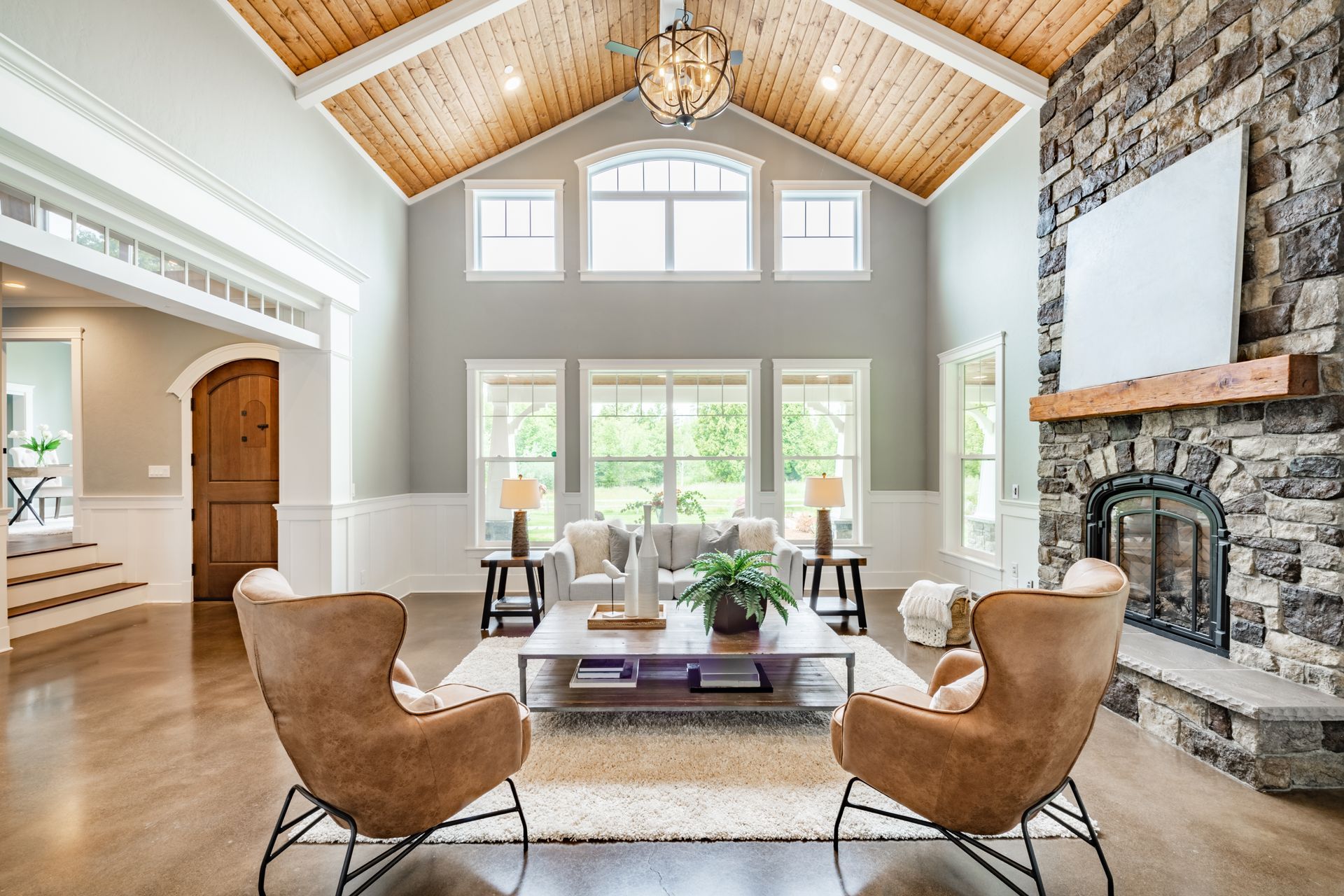 Living room with stone fireplace, wooden ceiling, and brown leather chairs.