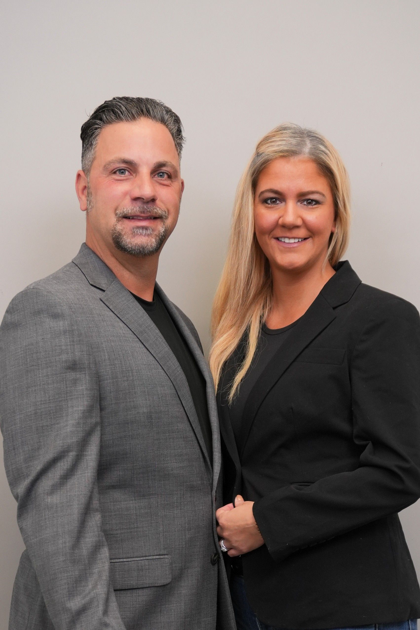 Man and woman, posing together, wearing business attire, against a plain background.