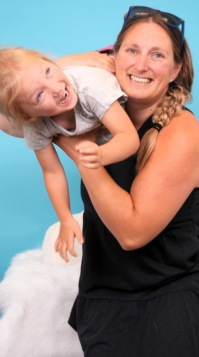 Woman smiling, holding a laughing child against a blue backdrop.