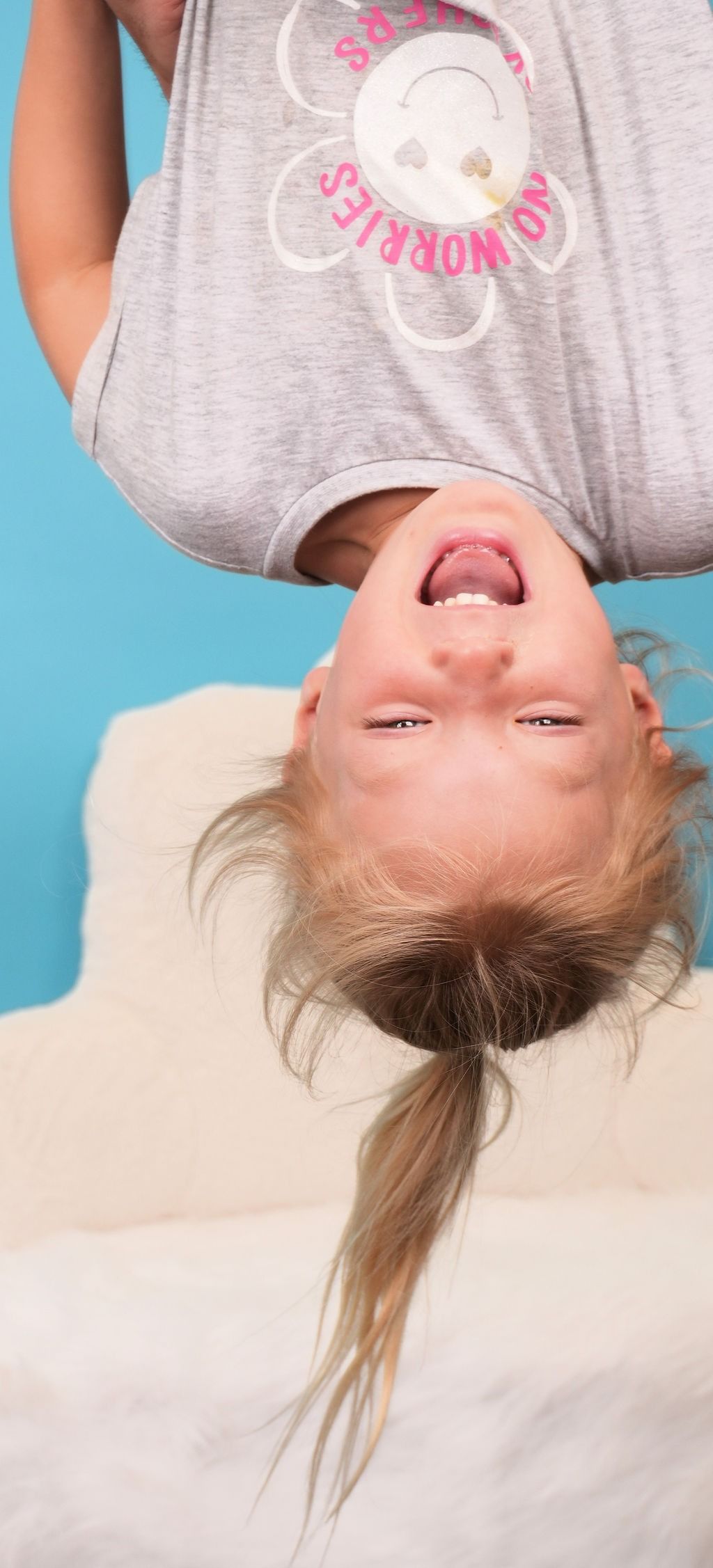 A girl with blonde hair in a ponytail is upside down, laughing, and wearing a gray shirt.
