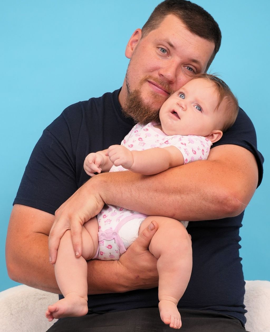 Man holding a baby. Man is smiling, baby looking up. Blue background.