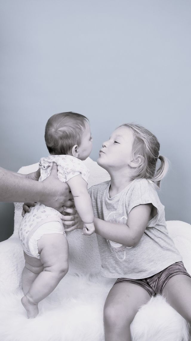 Older child kissing baby held by an unseen person.
