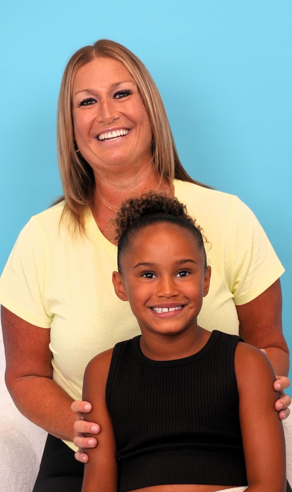 Woman and child smiling at the camera, woman's arm around child's shoulders. Against a blue background.