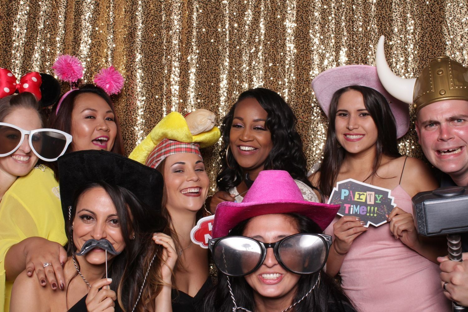 Group of people posing with props in front of a gold sequin backdrop, smiling and laughing.