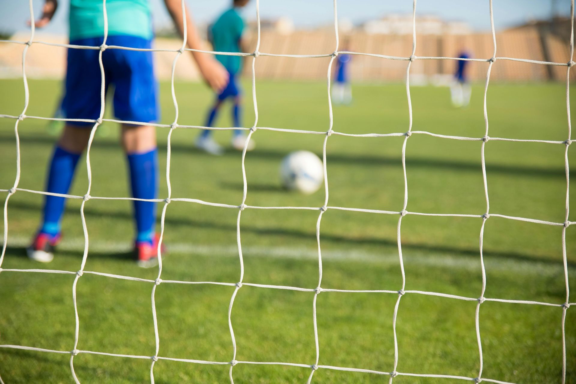 Soccer players on a green field; net in foreground.
