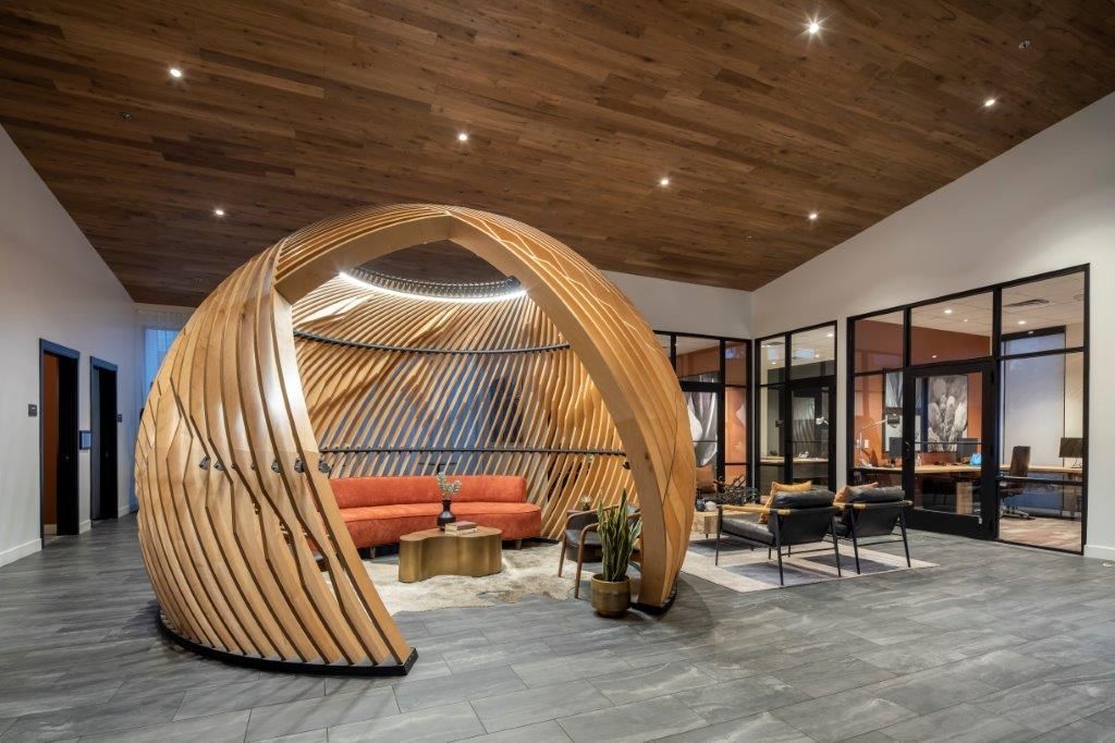 Modern lobby area featuring a large curved wooden seating pod and glass-walled meeting rooms.