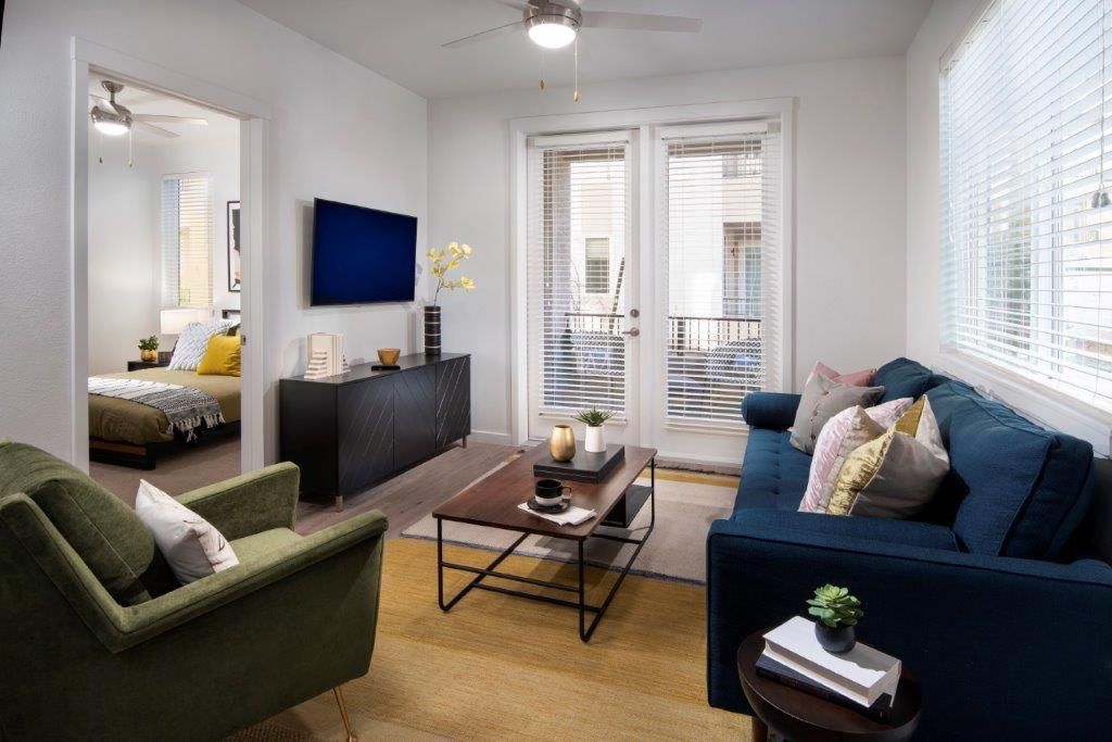Living room in an apartment with a blue sofa, green chair, coffee table, TV, and balcony doors.