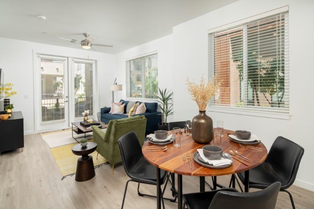 Open-concept apartment living and dining area with a round wood table, black chairs, and large windows.