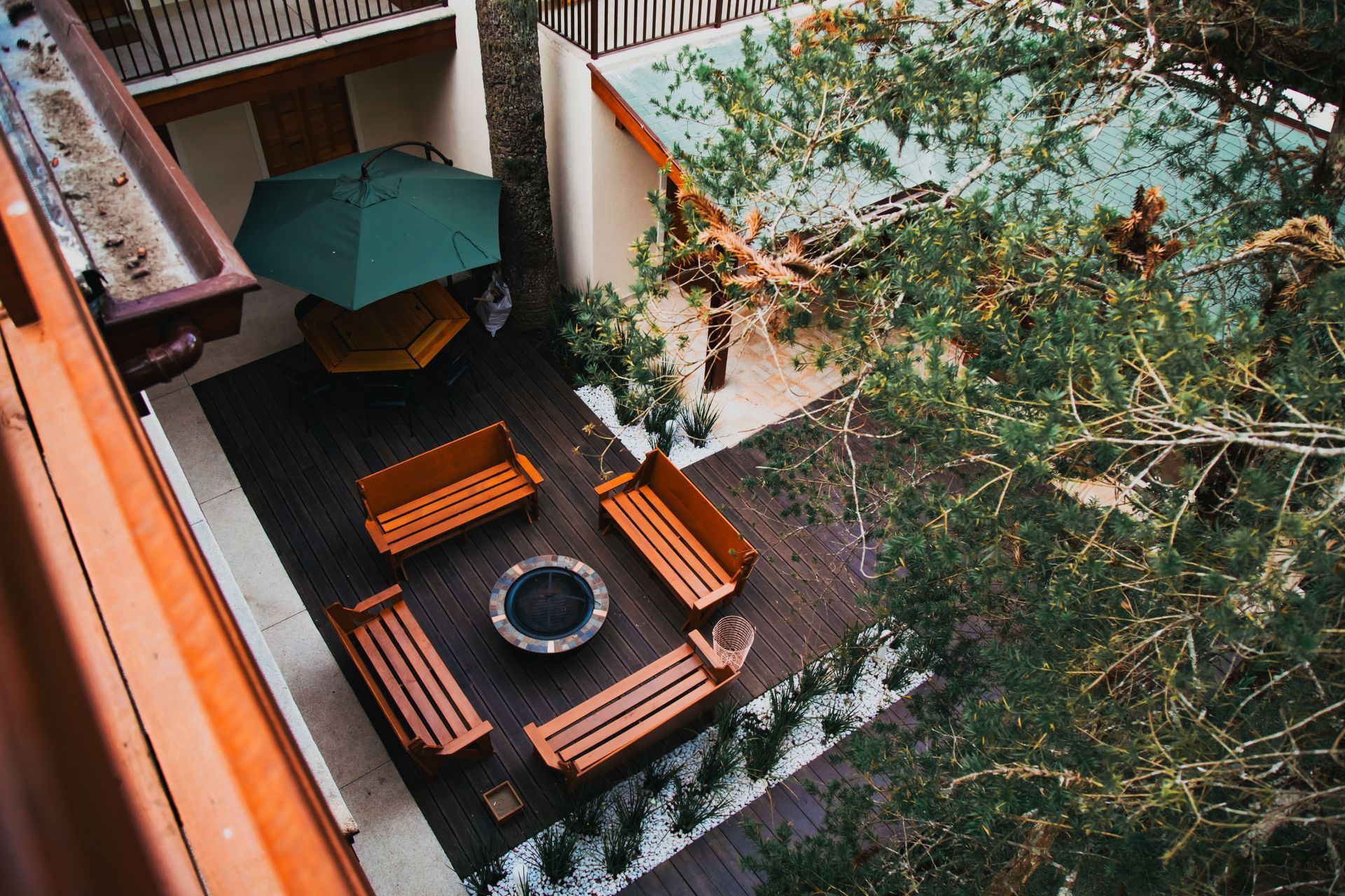 Courtyard seating area with benches, circular fire pit, green umbrella, and tree branches overhead