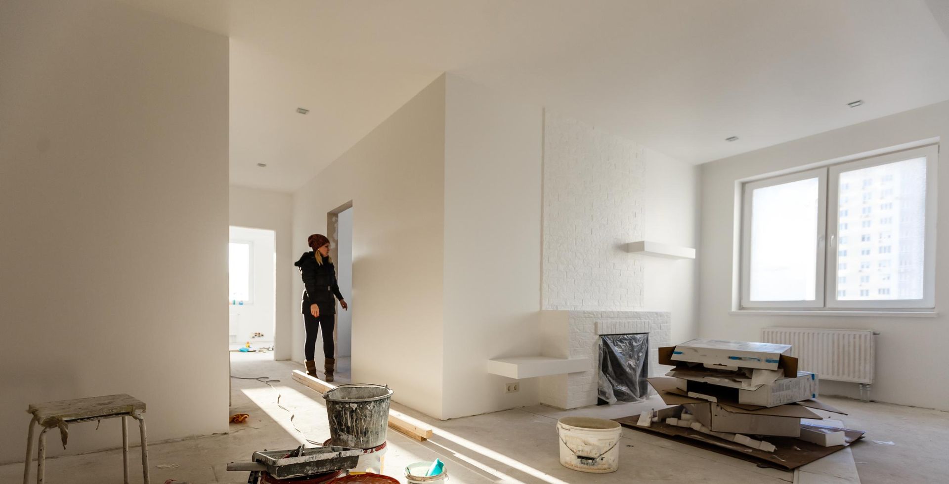 Woman in black clothing in white room under renovation, surrounded by tools and construction materials.