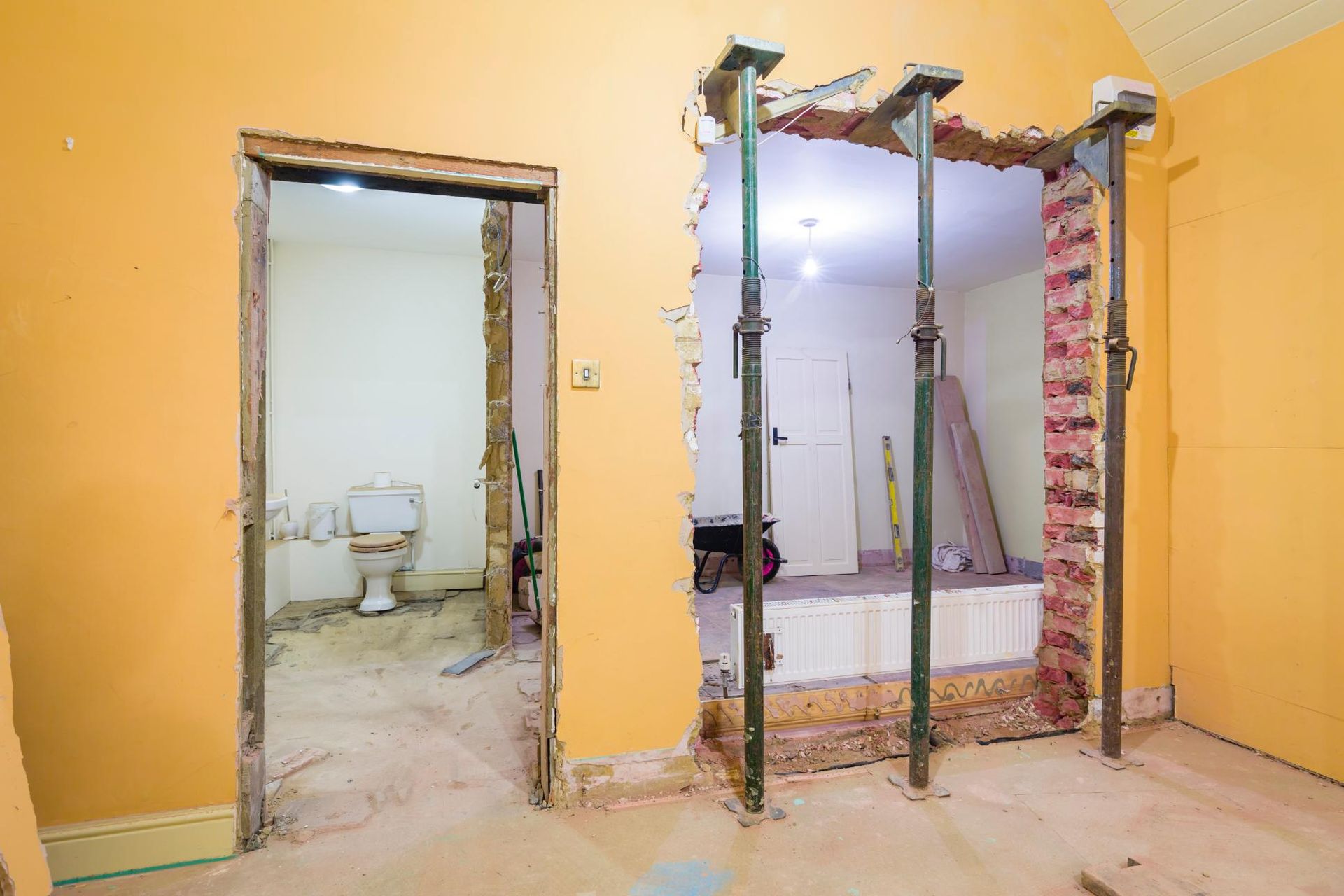 Renovation in progress: doorway to a bathroom with a toilet and doorway opening held up by support posts.