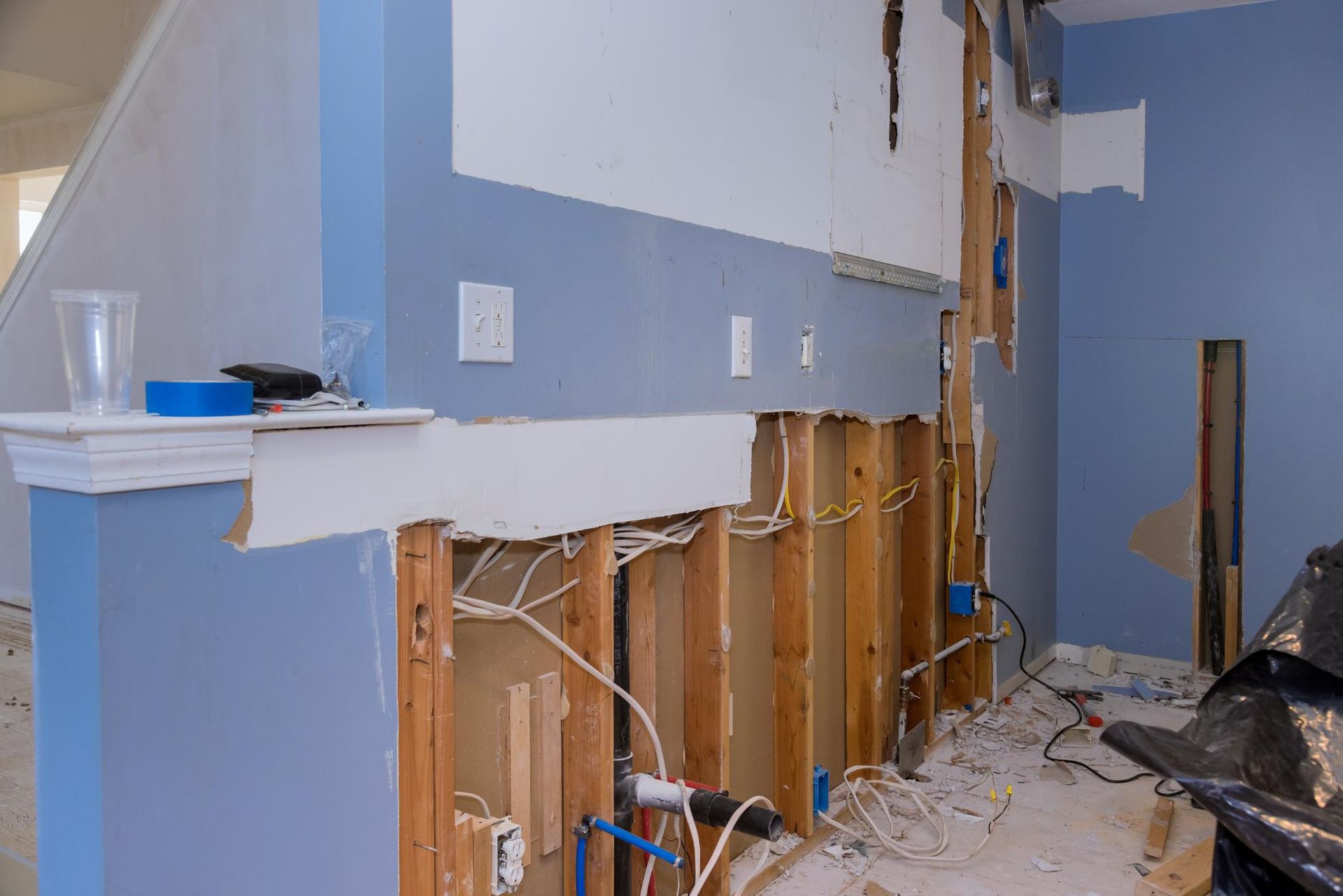 Interior wall with exposed studs, electrical wiring, and plumbing during renovation; blue paint.