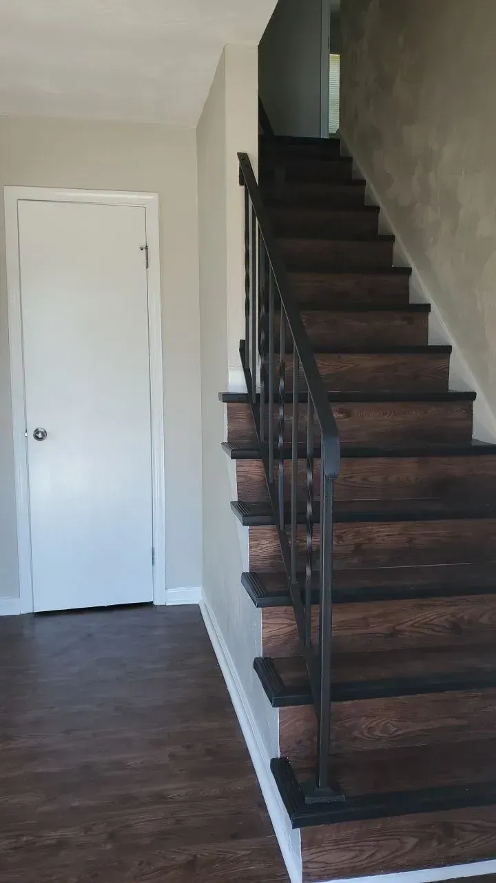 Staircase with dark wood steps and wrought iron railing, leading upwards. 